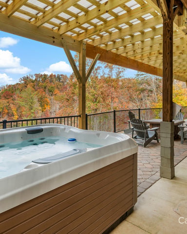 Hot tub on covered deck with fall foliage views, Adirondack chairs, and wooden pergola overhead