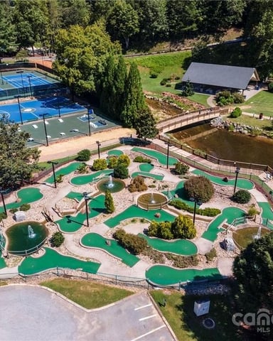Aerial view of resort with mini golf course, tennis courts, river, and manicured grounds surrounded by trees