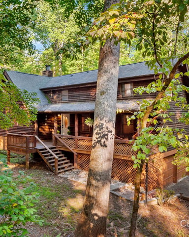 Rustic log cabin with wraparound deck nestled among tall trees in wooded setting