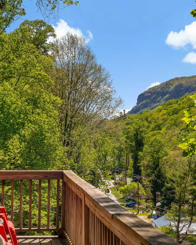 Wooden deck with red Adirondack chairs overlooking forested valley and distant mountain ridge