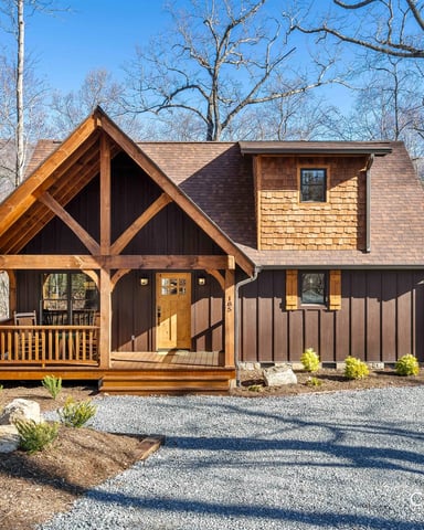 Modern timber-frame cabin with dark exterior, covered porch, and cedar shingle upper level surrounded by bare trees