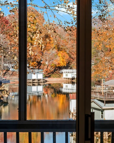View through windows of autumn lakeside landscape with fall foliage, docks, and houses reflected in calm water