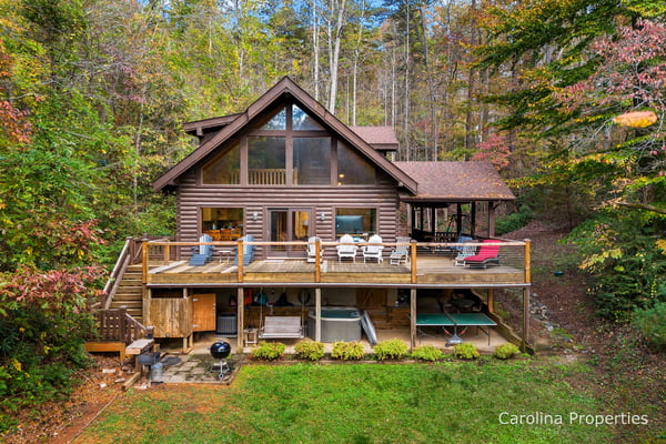 Modern log cabin with two-story deck, Adirondack chairs, and grill surrounded by autumn forest